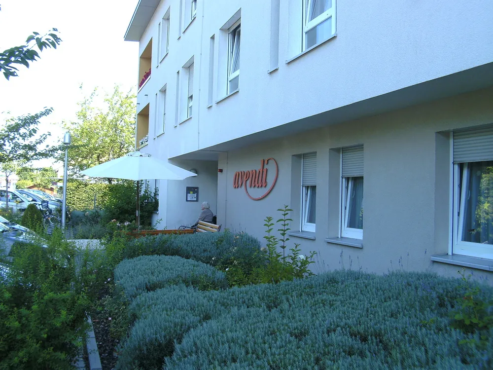 Haus mit dem Schriftzug avendi, davor Lavendelbeete und ein Sonnenschirm