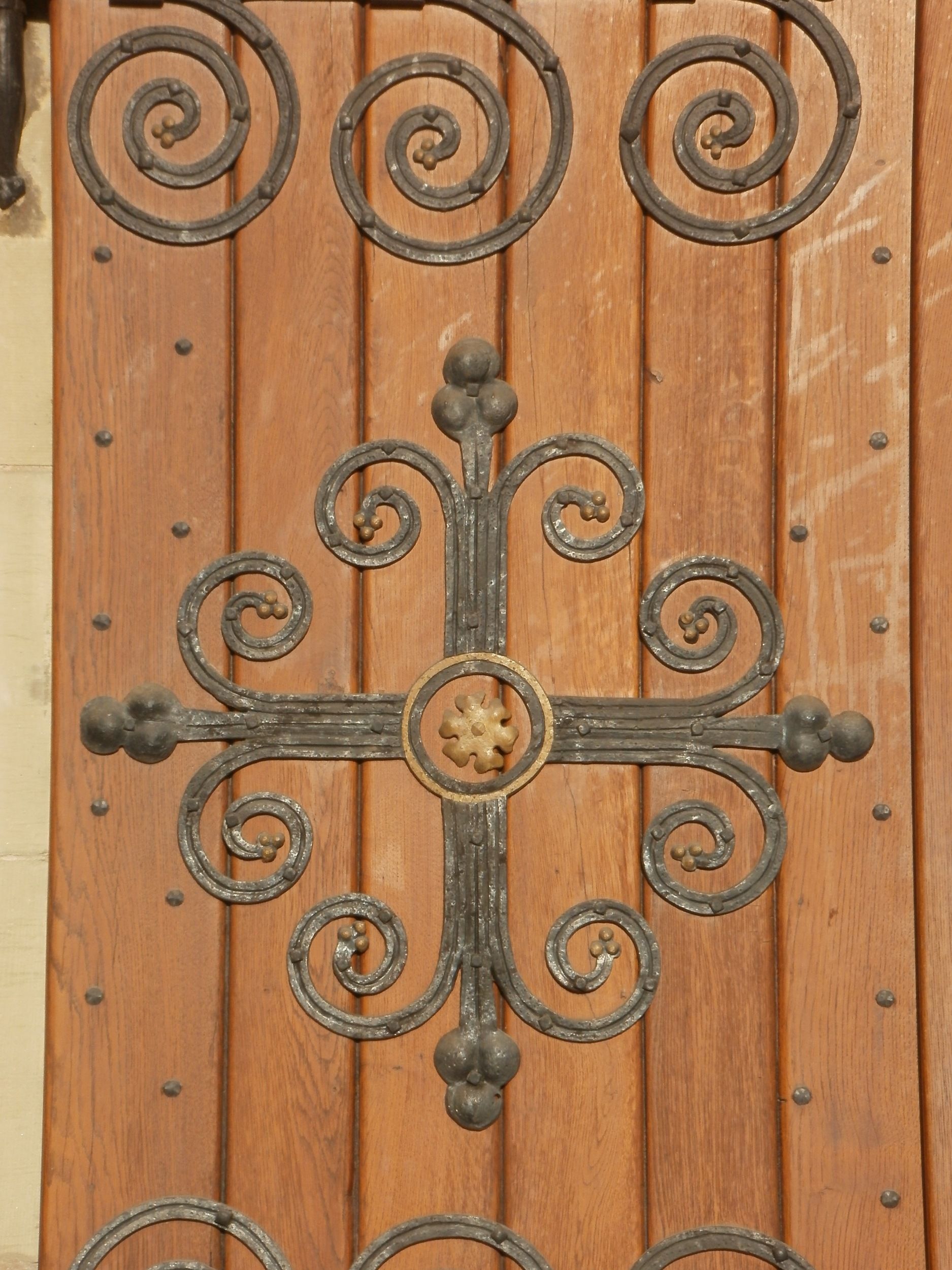 Holztür der Kirche Sankt Sebastian mit geschmiedetem Beschlag: ein Kreuz aus eisernen Voluten mit goldener Rosette in der Mitte